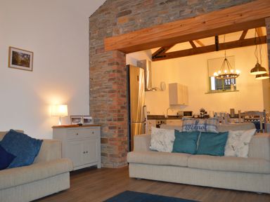 A living room with beige sofas and cushions next to a small cabinet with a lamp and photos at Cwrt y Wennol in Salem near Clydach