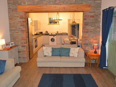 A living room with beige sofas and blue cushions next to a kitchen with white cabinets and dining table at Cwrt y Wennol Salem near Clydach
