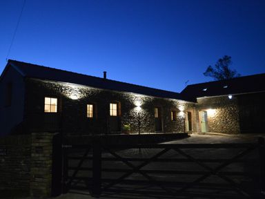 A stone building with illuminated windows and lights at night with a closed gate in front at Cwrt y Wennol Salem near Clydach