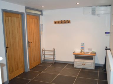 A hallway with two wooden doors a shoe rack a small cabinet with brochures and a coat rack on the wall at Cwrt y Wennol Salem near Clydach