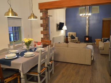 A combined dining and living area with a dining table set for six and a seating area with a fireplace at Cwrt y Wennol in Salem near Clydach
