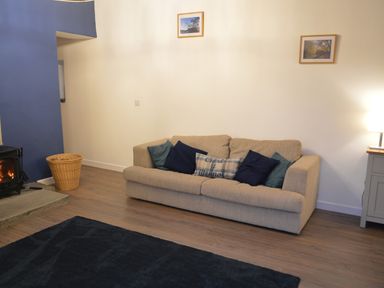 A living room with a beige sofa with pillows and a wood burning stove at Cwrt y Wennol Salem near Clydach