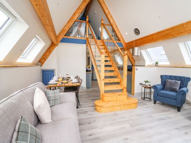 A living room with a gray sofa and blue armchair and dining table under a wooden staircase at Hill Radnor - The Sheepfold in Llanyre near Llandrindod Wells