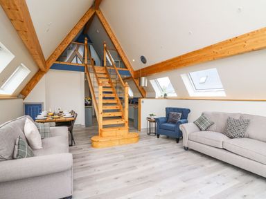 An attic living room with wooden beams two sofas an armchair a dining table and stairs leading to a loft at Hill Radnor - The Sheepfold in Llanyre near Llandrindod Wells