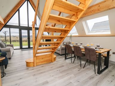 An open living and dining area with wooden staircase large windows two sofas and a dining table set with chairs at Hill Radnor - The Sheepfold in Llanyre near Llandrindod Wells