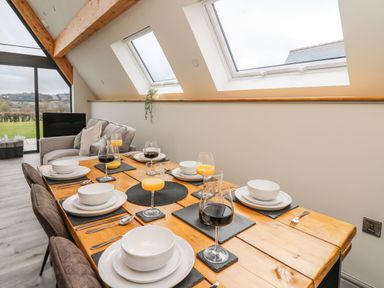 A dining table set with plates glasses and cutlery next to a seating area with a window wall at Hill Radnor The Sheepfold in Llanyre near Llandrindod Wells