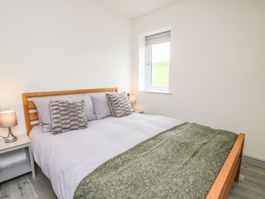 A bedroom with a wooden bed frame gray bedding and green blanket beside a window at Hill Radnor - The Sheepfold in Llanyre near Llandrindod Wells