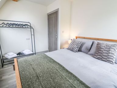 A bedroom with a wooden bed with gray bedding and pillows a metal clothes rack with hangers and folded towels and a closed door at Hill Radnor - The Sheepfold in Llanyre near Llandrindod Wells