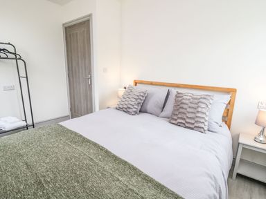 A bedroom with a double bed with pillows bedside tables with lamps a door and a clothes rack at Hill Radnor - The Sheepfold in Llanyre near Llandrindod Wells