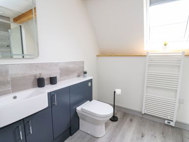 A bathroom with a sink, toilet, towel radiator, and a window at Hill Radnor - The Sheepfold in Llanyre near Llandrindod Wells