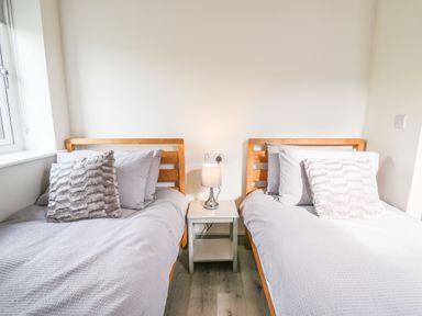 A bedroom with two single wooden beds with pillows and a nightstand with a lamp between them at Hill Radnor - The Sheepfold in Llanyre near Llandrindod Wells