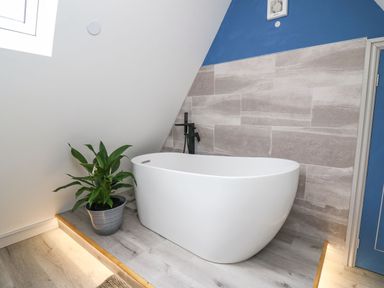 A modern bathroom with a white freestanding bathtub a potted plant on a raised platform and tiled wall at Hill Radnor - The Sheepfold Llanyre near Llandrindod Wells