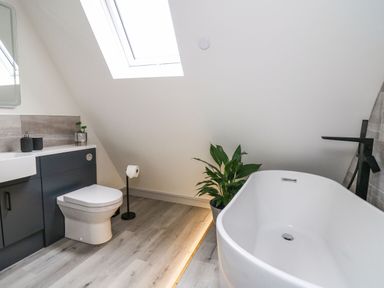 A bathroom with a white bathtub a toilet a sink with cabinet a skylight window and a plant at Hill Radnor - The Sheepfold in Llanyre near Llandrindod Wells