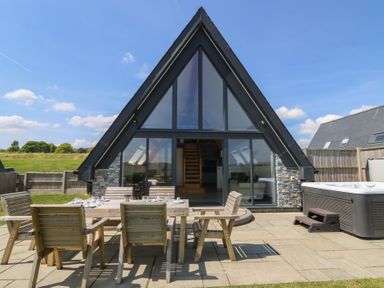 An outdoor patio with wooden table and chairs and a hot tub outside an a frame house at Hill Radnor - The Sheepfold in Llanyre near Llandrindod Wells