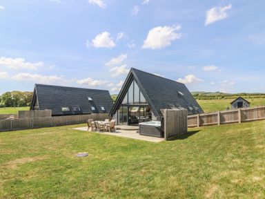 Two triangular houses with outdoor patio furniture and a hot tub in a grassy fenced yard at Hill Radnor - The Sheepfold in Llanyre near Llandrindod Wells
