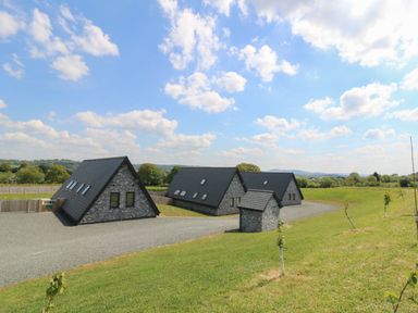 Three stone buildings with dark roofs on a gravel driveway surrounded by grass and small trees at Hill Radnor - The Sheepfold in Llanyre near Llandrindod Wells