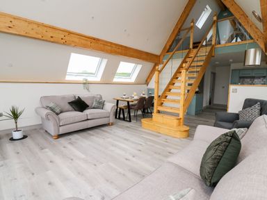 An open plan living room with sofas dining table and wooden staircase at Brecknock Cheviot - The Sheepfold in Llanyre near Llandrindod Wells