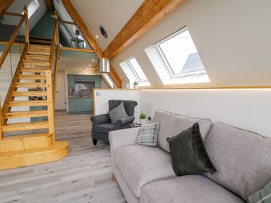 A living area with a gray sofa and armchair near wooden stairs and kitchen at Brecknock Cheviot - The Sheepfold in Llanyre near Llandrindod Wells