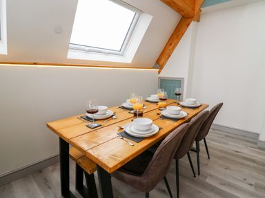 A dining table set with plates bowls glasses of juice and wine with chairs in a room with skylights and wooden beams at Brecknock Cheviot - The Sheepfold in Llanyre near Llandrindod Wells