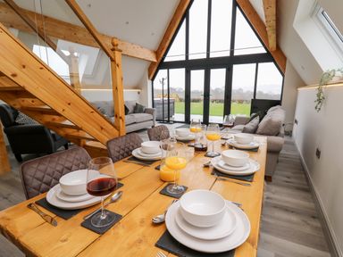 A dining table set with plates glasses and cutlery in a living area with sofas and large triangular windows at Brecknock Cheviot - The Sheepfold in Llanyre near Llandrindod Wells