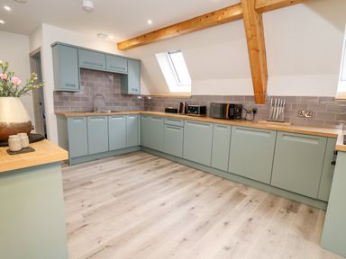 A kitchen with light green cabinets wooden countertops and gray tiled backsplash at Brecknock Cheviot - The Sheepfold in Llanyre near Llandrindod Wells