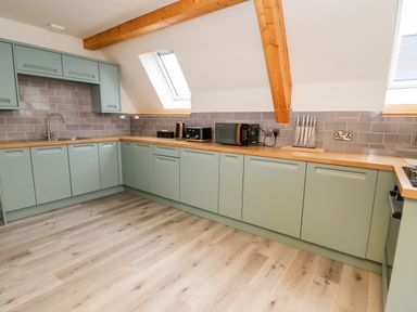 A kitchen with light green cabinets wooden countertops and appliances at Brecknock Cheviot - The Sheepfold in Llanyre near Llandrindod Wells