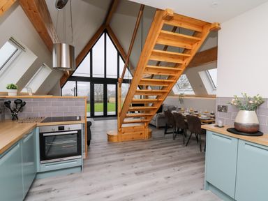 A kitchen and dining area with wooden stairs and large triangular windows at Brecknock Cheviot - The Sheepfold in Llanyre near Llandrindod Wells