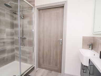 A bathroom with a glass shower enclosure a wooden door and a sink with cabinet at Brecknock Cheviot - The Sheepfold Llanyre near Llandrindod Wells
