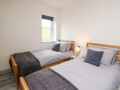 A bedroom with two single beds gray bedding and a nightstand with a lamp at Brecknock Cheviot - The Sheepfold in Llanyre near Llandrindod Wells