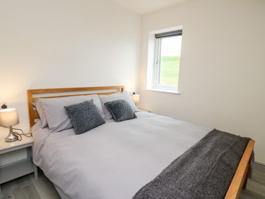 A bedroom with a wooden bed frame, gray bedding, two bedside tables with lamps, and a window at Brecknock Cheviot - The Sheepfold in Llanyre near Llandrindod Wells