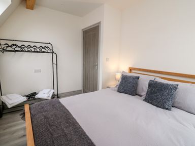 A bedroom with a double bed two pillows a bedside lamp a clothes rack with hangers and folded towels at Brecknock Cheviot - The Sheepfold in Llanyre near Llandrindod Wells