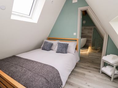 A bedroom with a bed and gray cushions next to a door leading to a bathroom at Brecknock Cheviot - The Sheepfold Llanyre near Llandrindod Wells