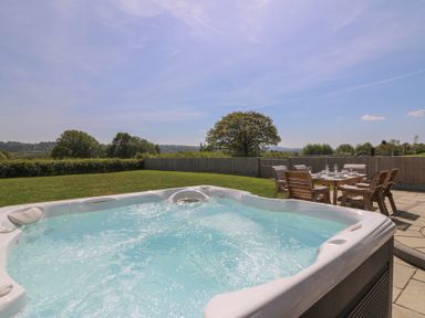 An outdoor area with a hot tub and a dining table with chairs on a patio at Brecknock Cheviot - The Sheepfold in Llanyre near Llandrindod Wells