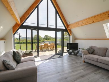 A living room with two sofas a television and large glass doors opening to an outdoor dining area at Brecknock Cheviot - The Sheepfold in Llanyre near Llandrindod Wells