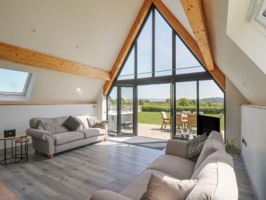 A living room with two sofas and a glass door opening to a garden at Brecknock Cheviot - The Sheepfold in Llanyre near Llandrindod Wells
