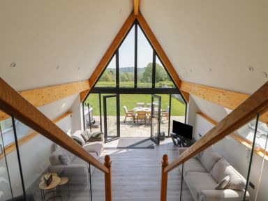 A living room with two sofas a television and glass doors leading to a patio with outdoor furniture at Brecknock Cheviot - The Sheepfold in Llanyre near Llandrindod Wells