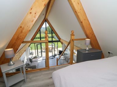 A bedroom loft overlooking a living room with a gray sofa and glass doors opening to a patio at Brecknock Cheviot - The Sheepfold in Llanyre near Llandrindod Wells