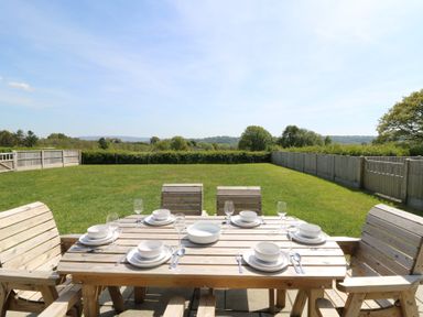 An outdoor wooden dining table set with plates bowls glasses and cutlery in a fenced grassy garden at Brecknock Cheviot - The Sheepfold in Llanyre near Llandrindod Wells