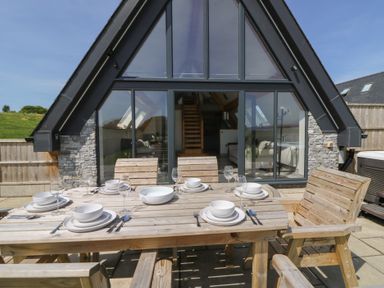 An outdoor wooden dining table set with plates and glasses in front of a modern a-frame house at Brecknock Cheviot - The Sheepfold in Llanyre near Llandrindod Wells