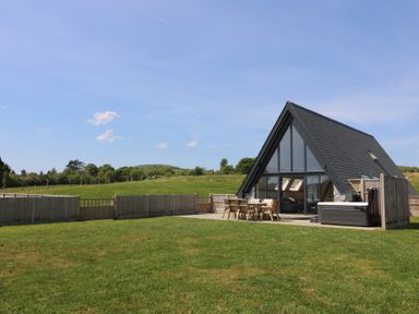 A fenced yard with a lawn and patio furniture outside an a frame house with large windows at Brecknock Cheviot - The Sheepfold in Llanyre near Llandrindod Wells