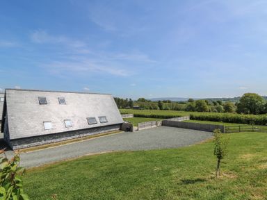An exterior view of a building with a sloped roof surrounded by grass and fenced areas at Brecknock Cheviot - The Sheepfold in Llanyre near Llandrindod Wells