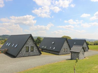 Three stone houses with black roofs on a gravel driveway in a green rural area at Brecknock Cheviot - The Sheepfold in Llanyre near Llandrindod Wells