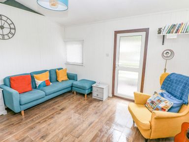 A living room with a blue sofa with colorful cushions a yellow armchair with cushions and a blue throw a small side table and a wooden floor at Doirewood Penlan Holiday Park near Cenarth