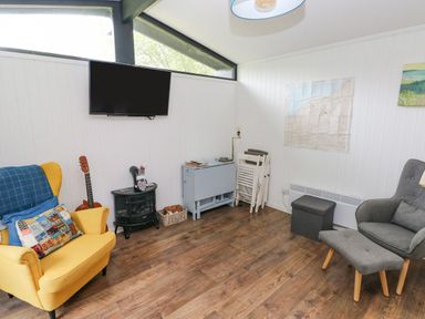 A living room with yellow and gray chairs a television mounted on the wall and a guitar at Doirewood in Penlan Holiday Park near Cenarth