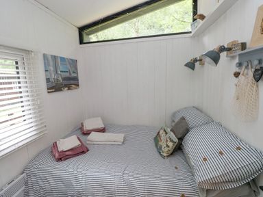 A small bedroom with a bed with striped bedding and folded towels on it at Doirewood in Penlan Holiday Park near Cenarth