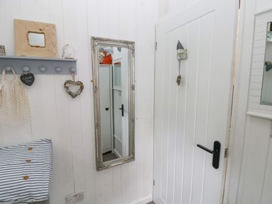 A white door with a black handle and a hanging ornament next to a wall with a mirror a grey coat rack a striped pillow and heart decorations at Doirewood Penlan Holiday Park near Cenarth