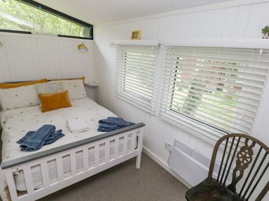 A small bedroom with a white wooden bed a chair and windows with blinds at Doirewood Penlan Holiday Park near Cenarth
