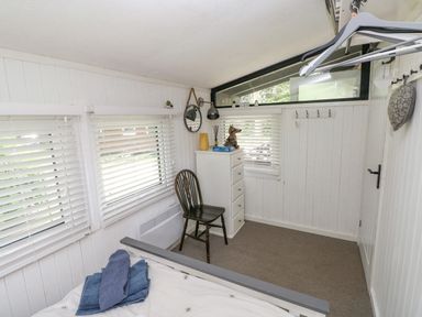 A small bedroom with a bed a wooden chair a white chest of drawers and windows with blinds at Doirewood Penlan Holiday Park near Cenarth