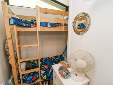 A small room with wooden bunk beds blue bedding a white dresser with a fan and a round mirror on the wall at Doirewood in Penlan Holiday Park near Cenarth