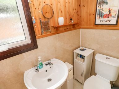 A bathroom with a sink a toilet a small cabinet and a window at Doirewood Penlan Holiday Park near Cenarth